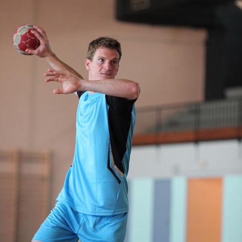 Junger Handballspieler im blauen Trikot wirft einen Ball in einer Sporthalle.