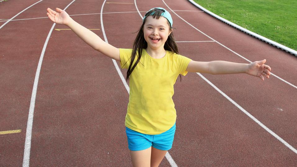 Lächelndes Mädchen in gelbem T-Shirt und blauen Shorts, läuft freudig auf einer Tartanlaufbahn.