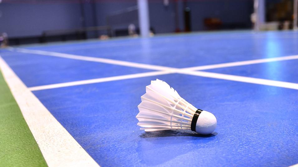 Nahaufnahme eines Federballs auf einem blauen Badmintonfeld mit weißen Linien.