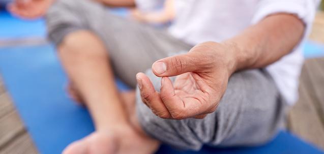 Nahaufnahme einer Hand, die im Meditationszustand auf einer blauen Yogamatte liegt, mit Fuß im Vordergrund.